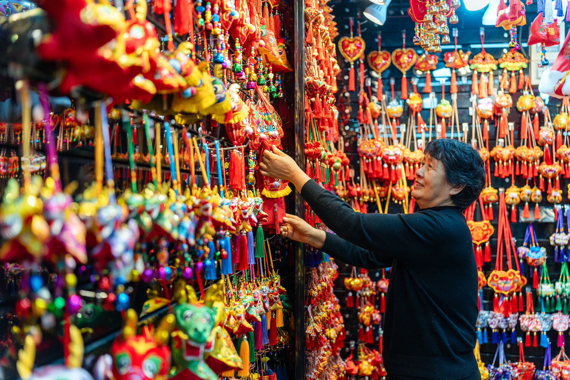 2023年12月11日，金華義烏國(guó)際商貿(mào)城，龍年喜慶用品掛滿攤位，顧客正在挑選中。